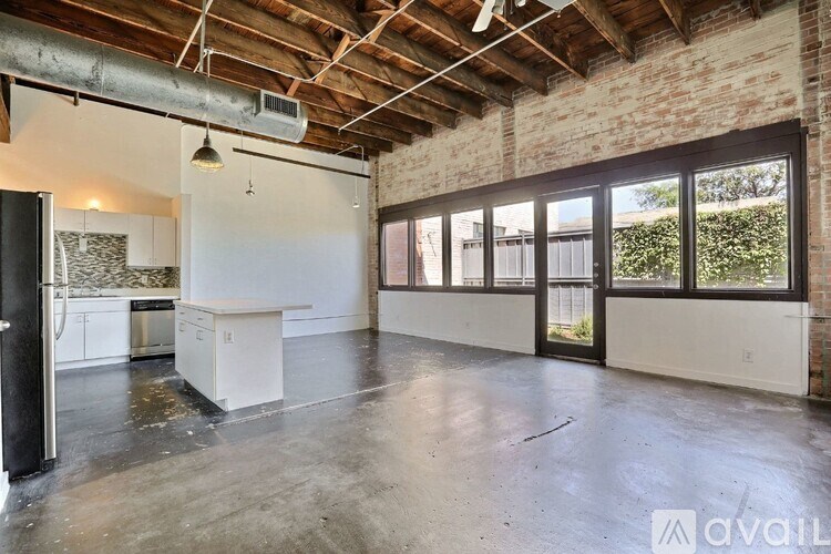 A large empty room with a kitchen area to the left and a door to the right.