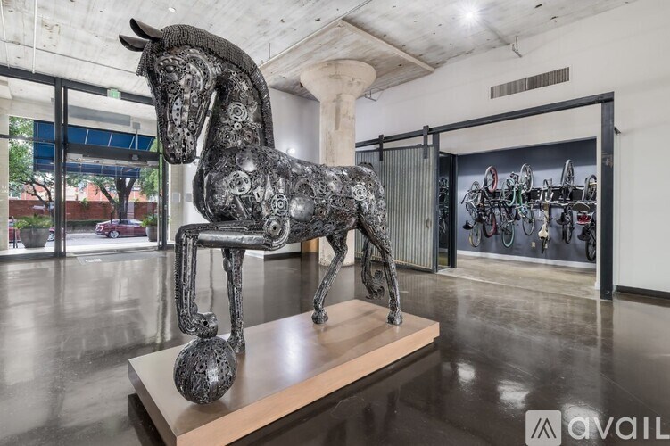 A large, metallic sculpture of a horse is displayed on a wooden platform in a spacious room.