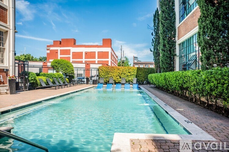 A pool surrounded by green bushes and trees with a red building in the background.