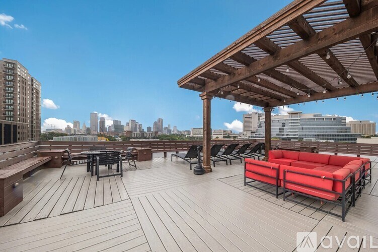 A wooden deck with red couches and a table is set up on a rooftop with a city skyline in the background.
