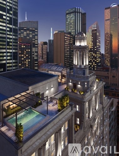 A tall building with a pool on the roof is lit up at night.
