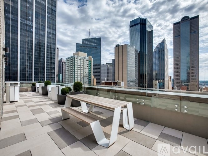 A modern outdoor seating area with benches and potted plants on a rooftop terrace overlooking a city skyline.