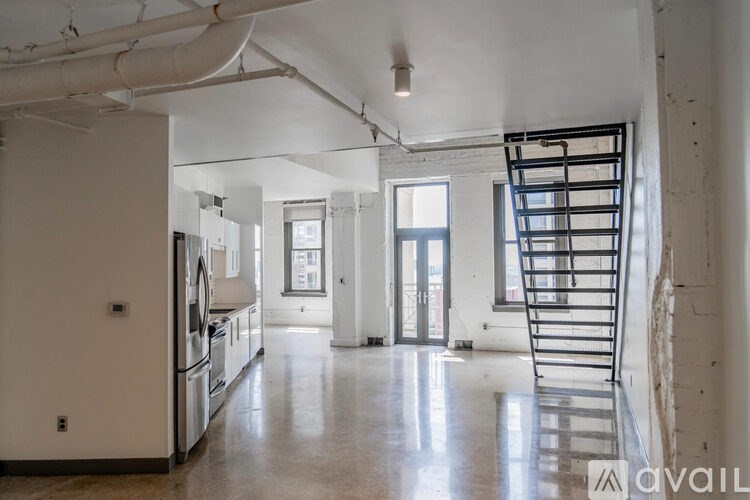 A large, empty room with a staircase and a kitchen area.