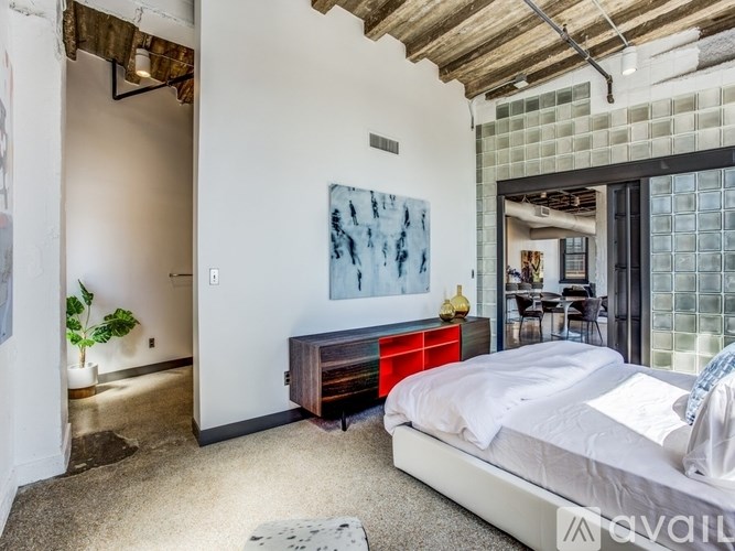 A bedroom with a bed, a painting, and a glass block wall.