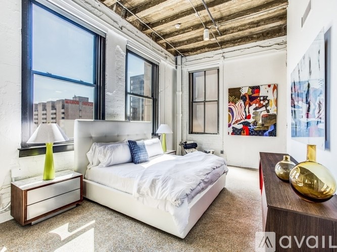 A bedroom with a large bed, a nightstand with a lamp, and a painting on the wall.