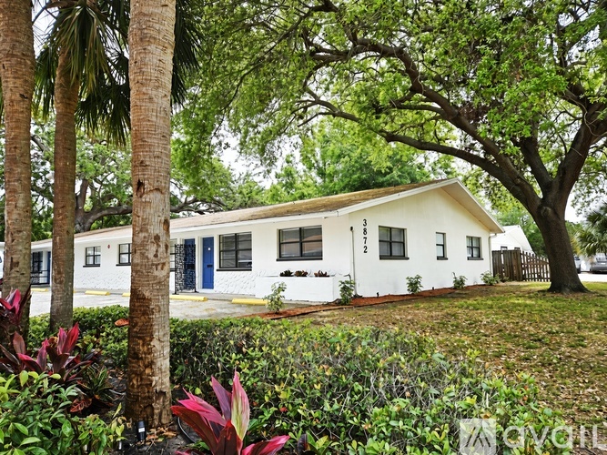 A white house with a blue door is surrounded by trees and plants.