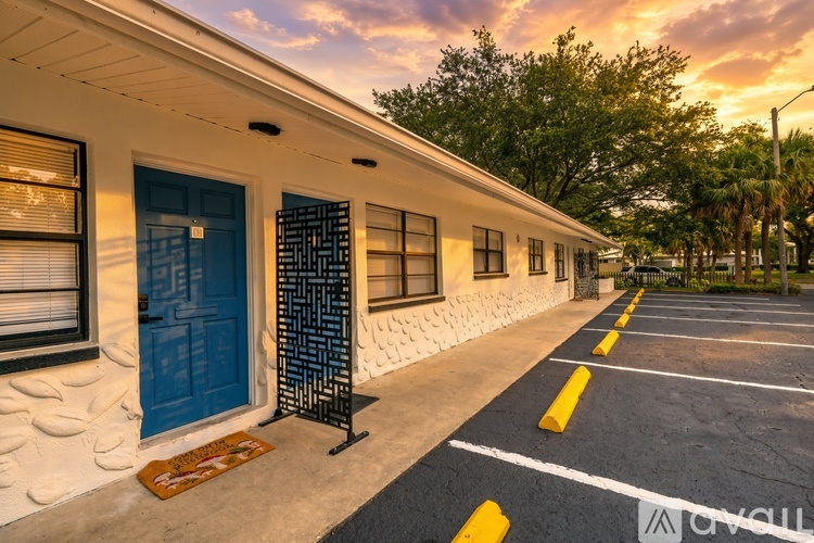 A sunset view of a building with a blue door and a parking lot in front.