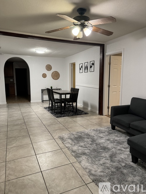 A living room with a black couch, a dining table with chairs, and a ceiling fan.