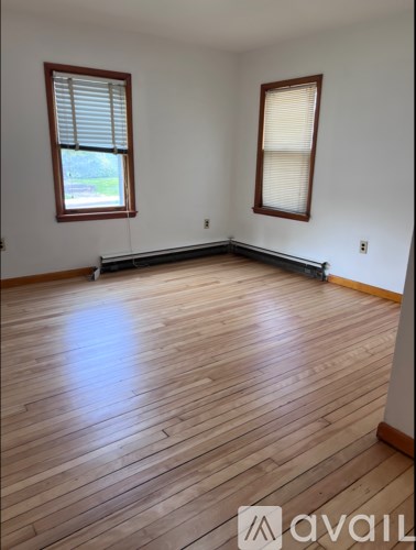 A room with wooden flooring and two windows.