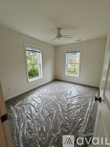 A room with a ceiling fan and two windows covered in plastic.