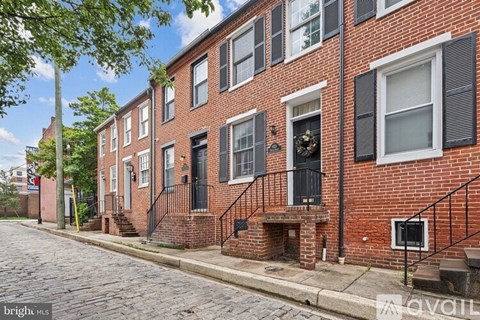 A row of red brick townhouses with black shutters and a cobblestone street.