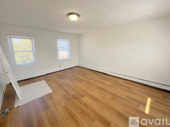 A room with wooden flooring and two windows.