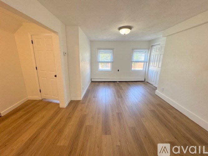 A room with wooden flooring and two windows.