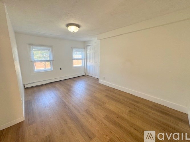 A room with wooden flooring and two windows.