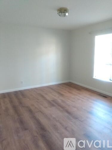 A room with wooden flooring and a window letting in sunlight.