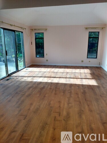 A room with wooden flooring and two windows.