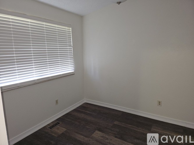 A room with a window covered by white blinds and a wooden floor.