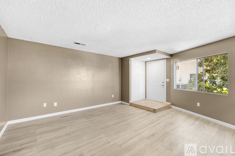 A room with a white door and a window with a view of trees.