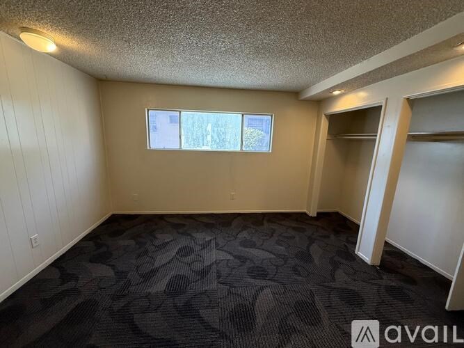 A room with brown walls and wooden flooring, with a window showing a view of trees and a house.