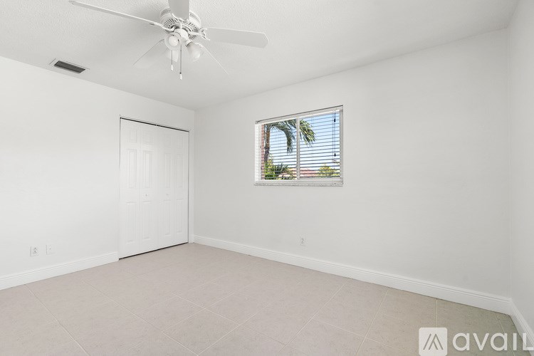A room with a ceiling fan and a window showing a palm tree outside.