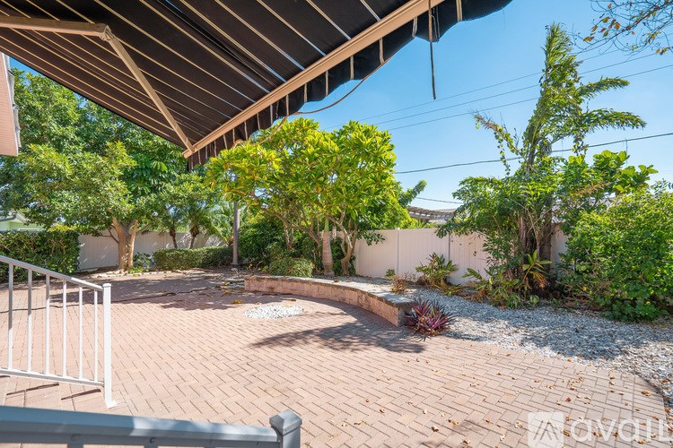 A backyard with a brick patio and a white fence.