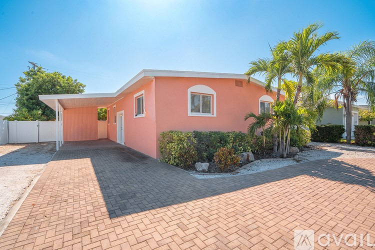 A pink house with a driveway and palm trees in front.