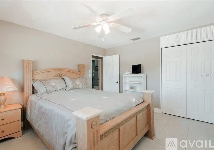 A bedroom with a large bed, a ceiling fan, and a nightstand with a lamp.