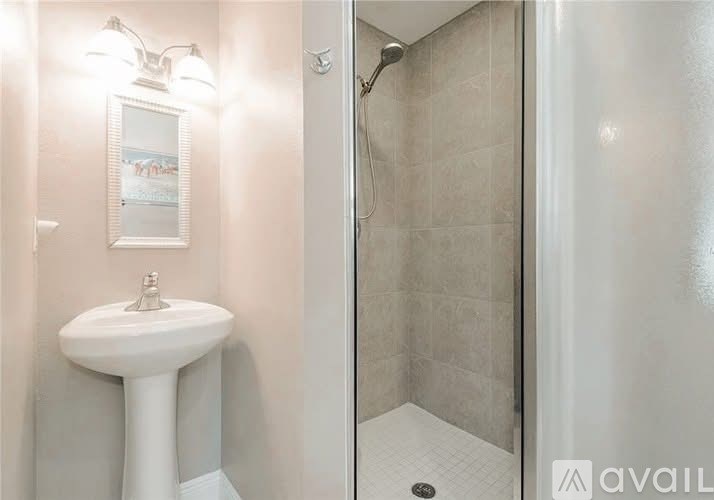 A white pedestal sink in a bathroom with a shower area.