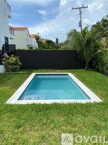 A small pool in a backyard with a white fence and green grass.