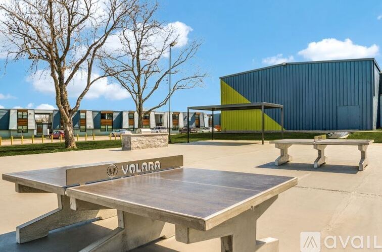A large table with the word "VALORA" on it is in the foreground of an outdoor setting with a modern building in the background.