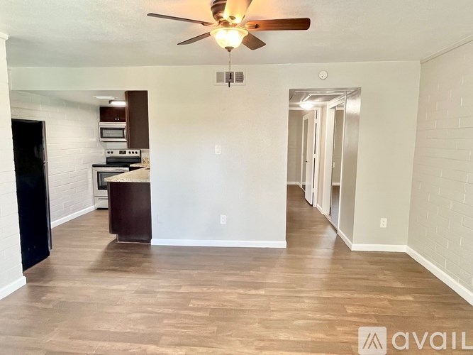 A spacious living room with a ceiling fan and a kitchen area in the background.