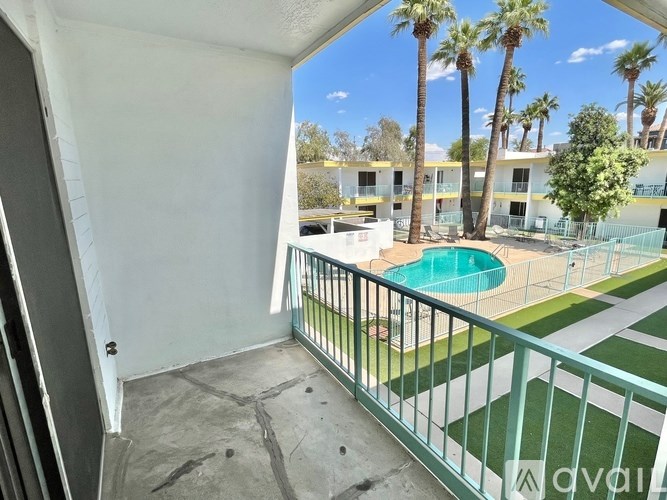 A balcony with a pool and palm trees in the distance.