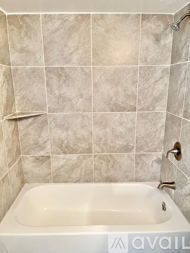 A white bathtub is in a bathroom with tiled walls.