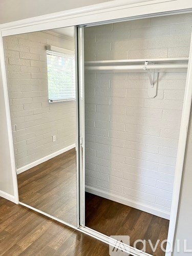 A white closet with a mirror door and a wooden floor.