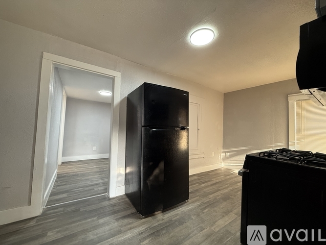 A black refrigerator in a room with wooden flooring and a white door.