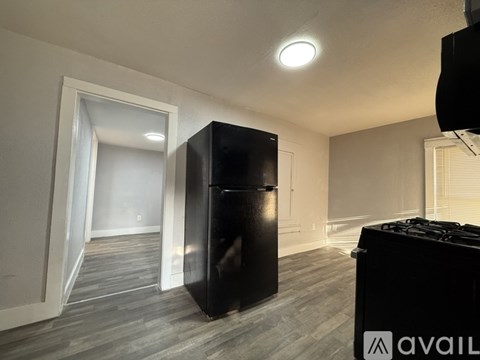 A black refrigerator in a room with wooden flooring and a white door.