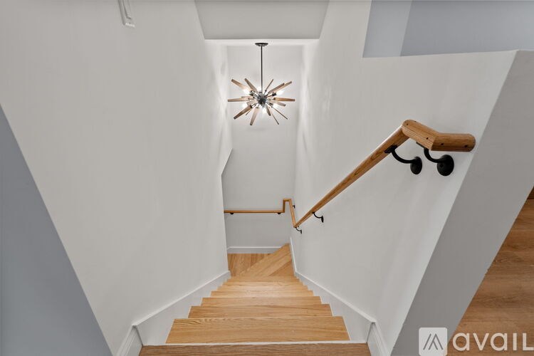 A staircase with a wooden handrail and a chandelier hanging from the ceiling.