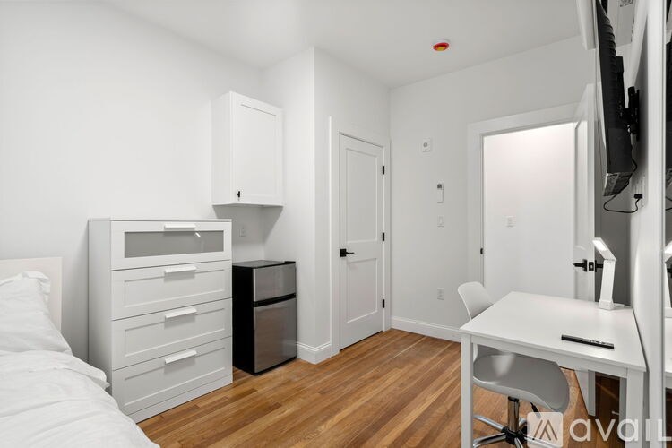 A white bedroom with a bed, desk, and drawers.