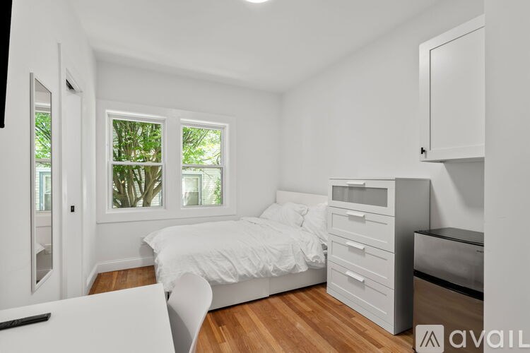 A white bedroom with a bed, drawers, and a cabinet.