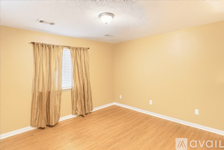 A room with a window covered by curtains and wooden flooring.