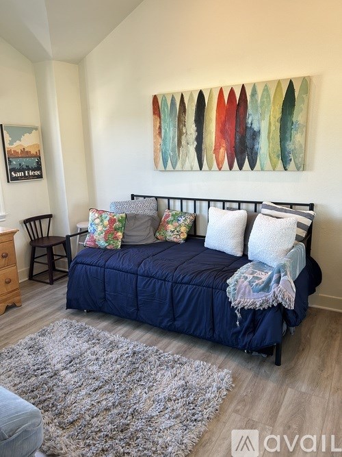 A bedroom with a blue bed and a painting on the wall.