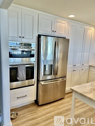 A stainless steel refrigerator stands in a kitchen with white cabinets.