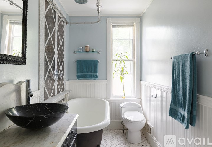 A bathroom with a black bowl sink, white toilet, and a window with a plant in it.