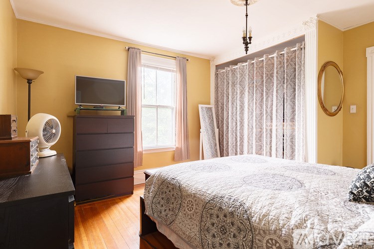 A bedroom with a bed, a dresser, and a window with curtains.
