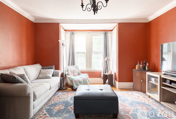 A living room with a white couch, a grey ottoman, and a chandelier.