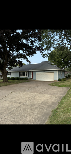 A house with a grey roof and a white garage door is surrounded by a grassy lawn.