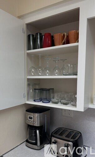 A kitchen cabinet with glasses and cups on the shelf.