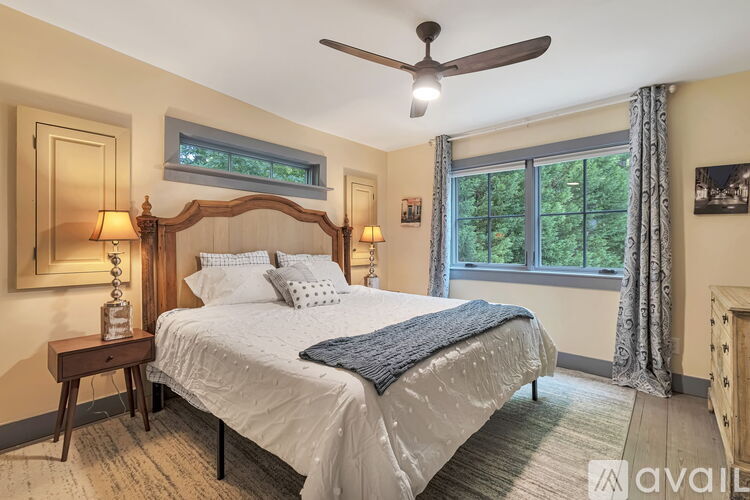 A bedroom with a large bed, a ceiling fan, and a window with a view of trees.