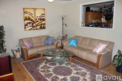 A living room with a tan couch, a glass coffee table, and a painting on the wall.