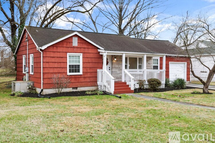 A red house with a white porch and a green lawn.